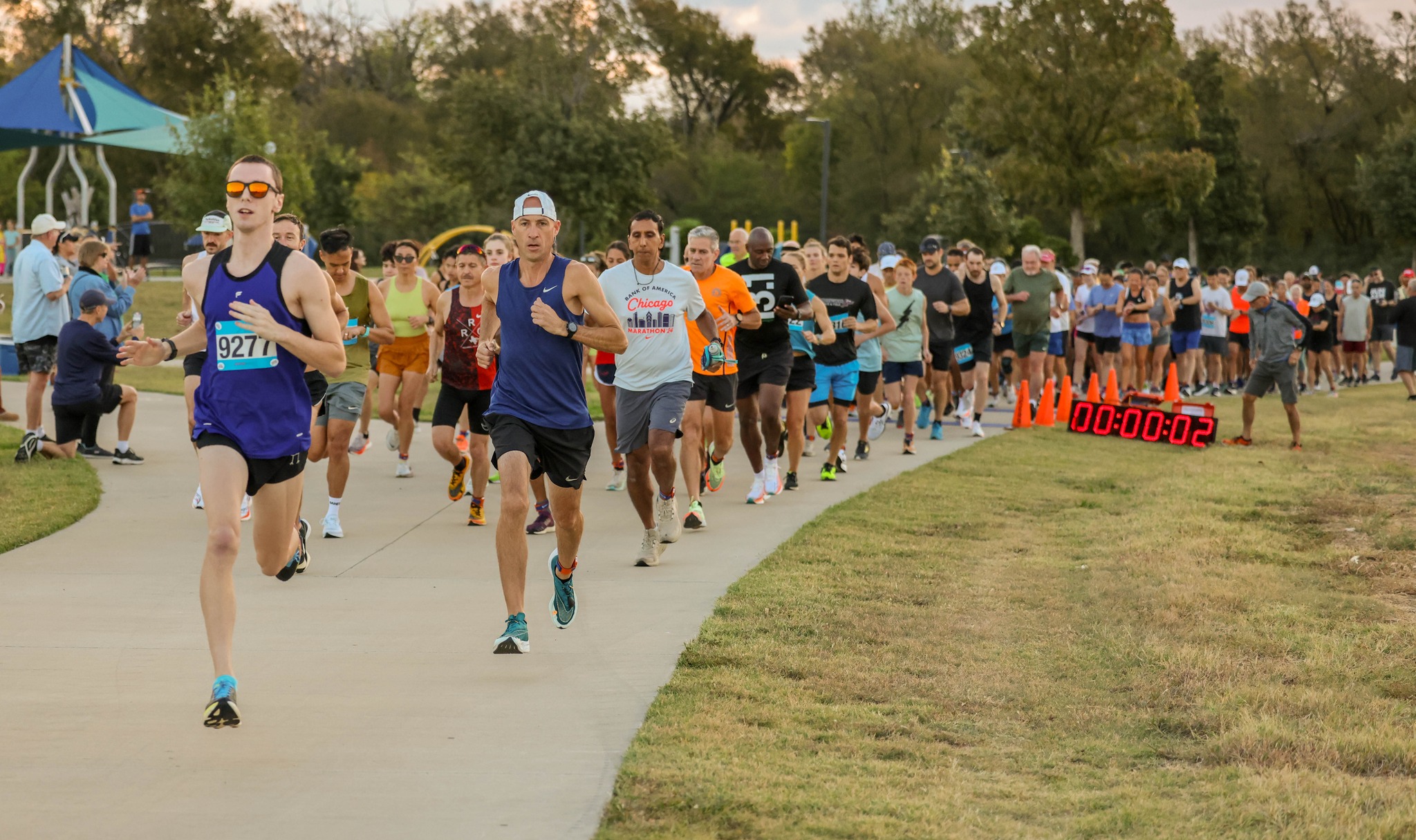 Runners starting a race in a park with spectators and a playground in background